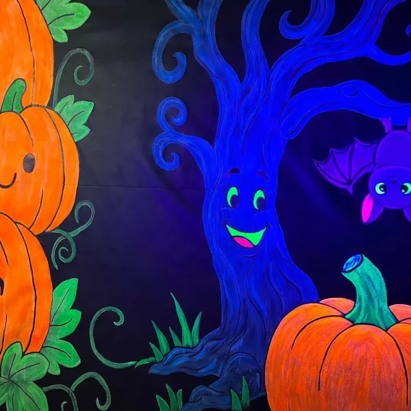 Blacklight illustration of smiling orange pumpkins, a friendly blue tree, and a purple bat hanging from a branch