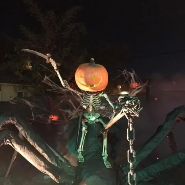 Outdoor Halloween display featuring a skeleton with a glowing jack-o'-lantern head riding a giant spider