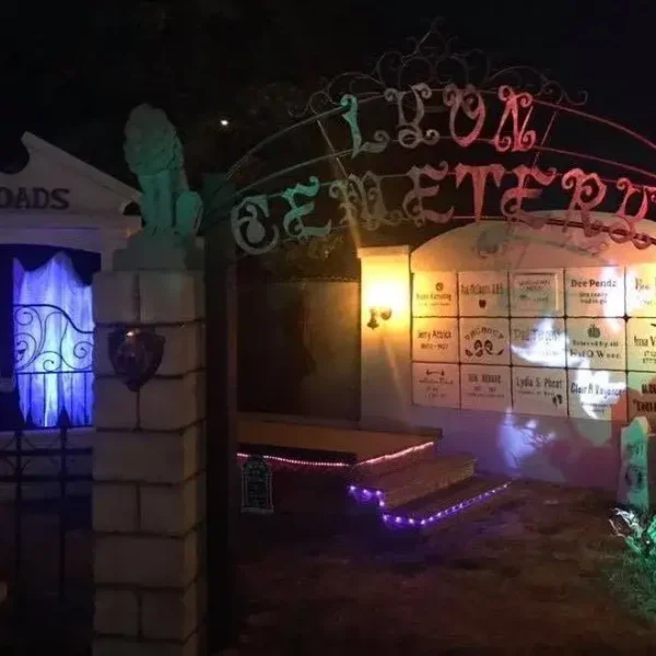 Halloween cemetery display at night with a decorative archway reading Lyon Cemetery illuminated by colorful eerie lights